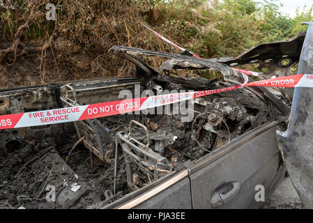 Fire damaged car showing the Fire & Rescue Service Do Not Cross plastic ribbon. Stock Photo