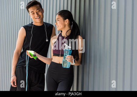 smiling asian sportswoman holding bottle of water and giving jump rope to young sportsman at street Stock Photo