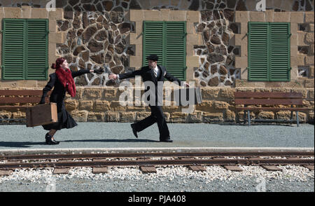 Young couple with vintage suitcase running fast outside a train station to catch the last train for journey. Stock Photo