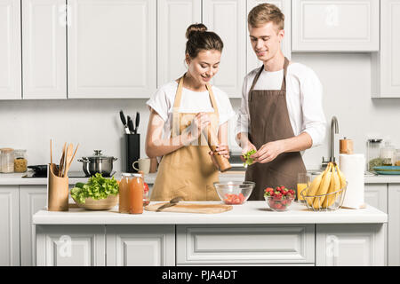 young couple cooking salad and adding spices in kitchen Stock Photo