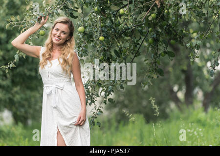happy stylish woman in white dress posing in orchard with apple trees Stock Photo