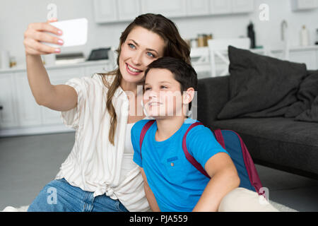 smiling mother and son with backpack taking selfie on smartphone together at home on first school day Stock Photo