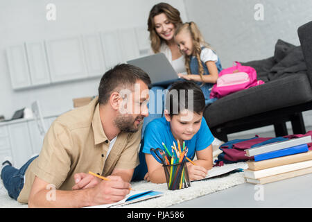 selective focus of father and son doing homework together while mother and daughter using laptop on sofa at home Stock Photo