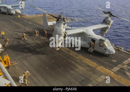 U.S. 5TH FLEET AREA OF OPERATIONS (July 3, 2018) U.S. Marines exit an MV-22B Osprey with Marine Medium Tiltrotor Squadron (VMM) 162 (Reinforced), 26th Marine Expeditionary Unit (MEU), after landing aboard the Wasp-class amphibious assault ship USS Iwo Jima (LHD 7), July 3, 2018. Iwo Jima is deployed in the U.S. 5th Fleet area of operations in support of naval operations to ensure maritime stability and security in the Central region, connecting the Mediterranean and the Pacific through the western Indian Ocean and three strategic choke points. Stock Photo