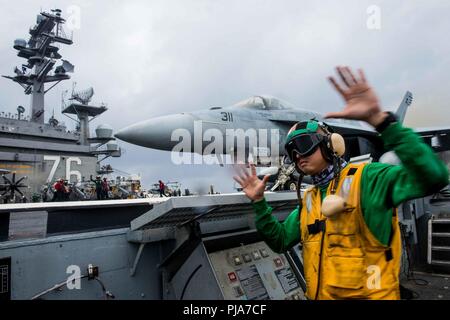 PHILIPPINE SEA (July 4, 2018)  Aviation Boatswain's Mate (Equipment) 1st Class Clayton Hudson, from Fairfield, Calif., signals for the launch of an F/A-18E Super Hornet assigned to Strike Fighter Squadron (VFA) 115 on the flight deck of the Navy's forward-deployed aircraft carrier, USS Ronald Reagan (CVN 76). Ronald Reagan, the flagship of Carrier Strike Group 5, provides a combat-ready force that protects and defends the collective maritime interests of its allies and partners in the Indo-Pacific region. Stock Photo