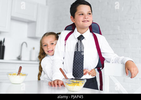 little sister hugging brother in school uniform with backpack at table with breakfast in kitchen at home, back to school concept Stock Photo