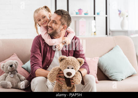 daughter hugging father on sofa with teddy bears at home Stock Photo