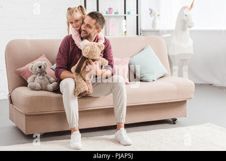 daughter hugging father on sofa with toys at home Stock Photo