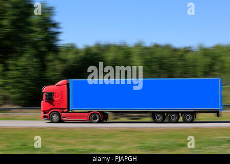 Side view of red semi truck in front of blue trailer at speed on motorway in the summer. Stock Photo