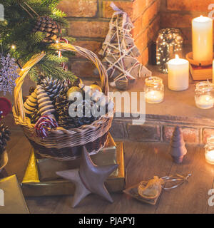 Christmas setting background, decorated Christmas tree, pine cones in the basket, wooden trees, poinsettia with fireplace on the background, candles a Stock Photo