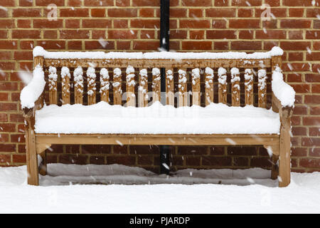 Wooden garden bench covered in snow against a brick wall Stock Photo