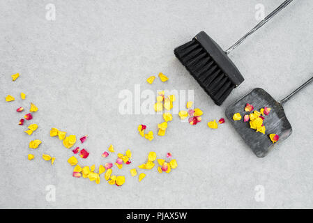 Sweeping away dry rose petals in the garden patio, with brush and dustpan, on concrete floor background. Change of seasons. Stock Photo