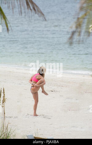 A young woman does a complex standing yoga pose with her leg in the air on the beach at Anna Maria Island, Florida. Stock Photo