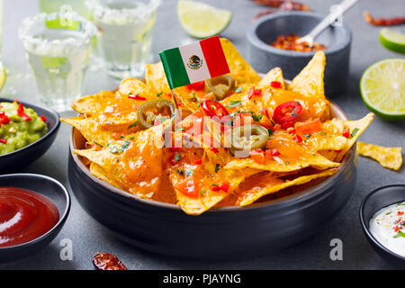 Nachos chips with Mexican flag and dips variety in black bowl. Grey stone background. Stock Photo