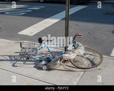 Trashed bike wrapped in garbage broken on street corner  Stock Photo