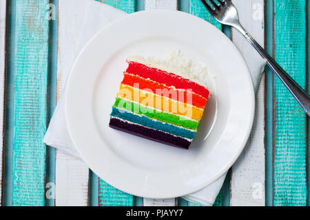 Rainbow cake on a white plate. Colorful wooden background. Top view. Stock Photo