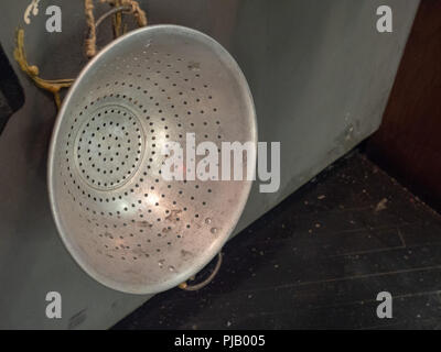 Rusty, stained metal colander hanging on wall with rope Stock Photo