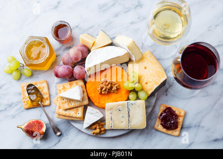 Assortment of cheese, grapes with red and white wine in glasses. Marble background. Top view. Stock Photo
