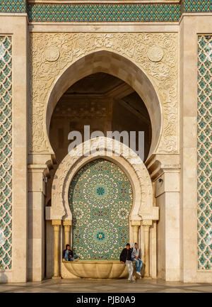 Casablanca, Morocco - December 09, 2012: Arabesque mosaic design on the fountain ot the Mosque Hassan II in and people sitting on it Stock Photo