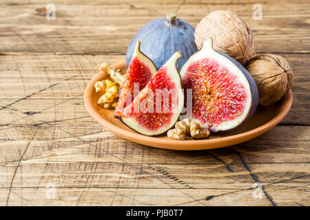 Fresh figs whole and cut kernels of walnuts on a plate the old wooden background Stock Photo