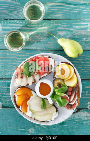 Plate with different sandwiches with fruit on wooden table with glasses of wine, top view. Snacks for wine concept. Bruschetta with fruit Stock Photo
