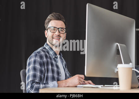 handsome smiling young programmer in eyeglasses working with desktop computer Stock Photo