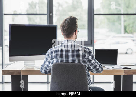 back view of young programmer working with laptop and desktop computer Stock Photo