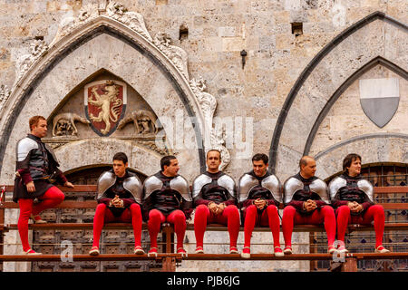 A Group Of Local Men Dressed In Medieval Costume Sit On Bleachers In The Piazza Del Campo After A Morning Trial Race, The Palio di Siena, Siena, Italy Stock Photo