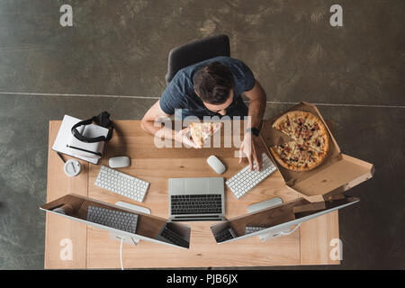 overhead view of programmer eating pizza and using computers at workplace Stock Photo