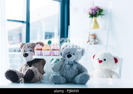 selective focus of teddy bears on table with cupcakes on stand Stock Photo