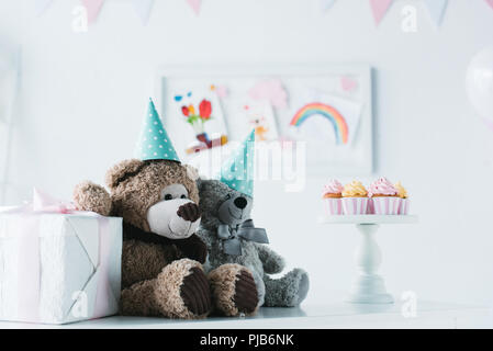 teddy bears in cones on table with cupcakes on stand and present box Stock Photo