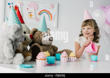 adorable birthday child having tea party with teddy bears in cones at table with cupcakes Stock Photo