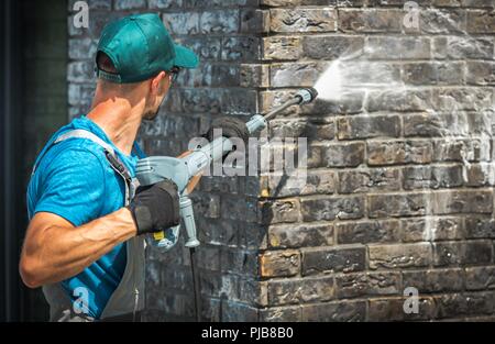 House Brick Wall Washing Using Pressure Washer. Caucasian Worker in His 30s. Stock Photo