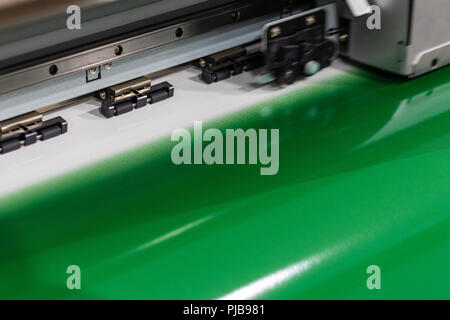 Big professional printer, processing a large scale green, glossy, vinyl roll. Stock Photo