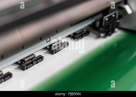 Big professional printer, processing a large scale green, glossy, vinyl roll. Stock Photo