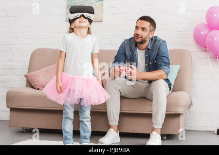 father and daughter using virtual reality headset and joystick at home Stock Photo
