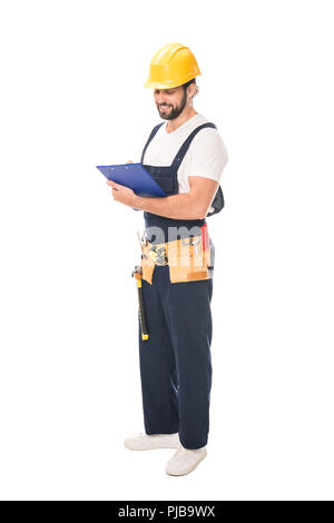 full length view of smiling workman in tool belt writing on clipboard isolated on white Stock Photo