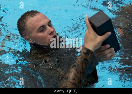 Lance Cpl. Noah Wishart, from Milwaukee, Wisconsin, grabs a brick from a Marine during the scout swimmers course July 12, 2018 at the Camp Hansen Aquatics Center, Okinawa, Japan. The scout swimmers course provides the Marine Corps with amphibious capabilities while teaching Marines to become proficient at long-distance swimming. Wishart is attached to Expeditionary Operations Training Group, III Marine Expeditionary Force Information Group. Stock Photo