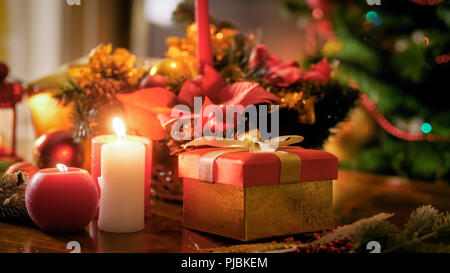 Closeup photo of candles and gifts on wooden table against Christmas tree Stock Photo