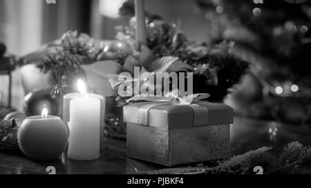 Black and white image of candles, gifts and baubles against Christmas tree Stock Photo