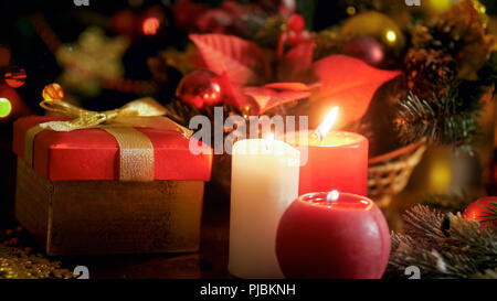Closeup photo of three candles burning next Christmas gifts and decorative wreath Stock Photo