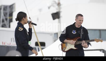 Senior Master Sgt. Matthew Ascione, right, U.S. Air Force Band Max Impact guitarist, plays alongside Tech. Sgt. Nalani Quintello, left, Max Impact vocalist, during a performance at Daytona International Speedway in Daytona Beach, Fl., July 6, 2018. Max Impact performed for the Coca-Cola Firecracker 250 and the Coke Zero Sugar 400, showcasing Air Force excellence to tens of thousands of attendees. Stock Photo