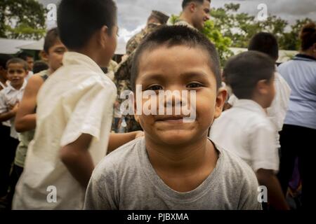 A local Guatemalan child poses for a photo while U.S. Marines conduct a site survey of the school he is attending in Flores, Guatemala, July 9, 2018. The Marines and sailors of SPMAGTF-SC are conducting security cooperation training and engineering projects alongside partner nation military forces in Central and South America. The unit is also on standby to provide humanitarian assistance and disaster relief in the event of a hurricane or other emergency in the region. Stock Photo