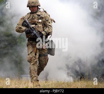 1st Lt. Jorge Acevedo, assigned to U.S. Army Garrison-Bavaria, uses a three-to-five  second rush technique under the cover of smoke to safely cross an open field during the 2018 21st Theater Sustainment Command Best Warrior Competition July 10, 2018 at Baumholder, Germany.  After covering a 100 meter distance, competitors completed a media engagement scenario where they were asked to respond to several questions while on camera.#21BWC18 #FirstInSupport #StrongEurope Stock Photo