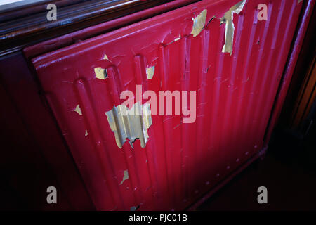 Peeling paint on a red and silver radiator in a pub in Bawtry, England Stock Photo