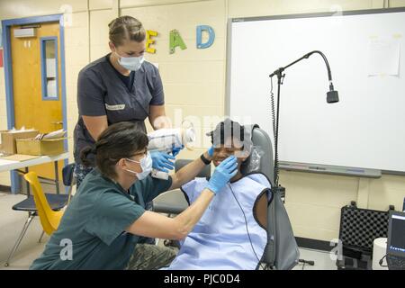 U.S. Air Force Tech. Sgt. Kay Ankerich, of Hartwell, Ga., a dental technician with the Air Force Reserve’s 94th Aeromedical Staging Squadron, Dobbins Air Reserve Base, Ga., prepares a young girl to take an x-ray while Navy Reserve Hospital Corpsman Petty Officer Second Class Kiara Schuster, of Stevens Point, Wisc., a general medic with the Expeditionary Medical Facility Great Lakes stands ready to take the x-ray during the East Central Georgia Innovative Readiness Training in Millen, Ga., July 14, 2018, An IRT provides hands-on, real-world training to improve readiness and interoperability for Stock Photo