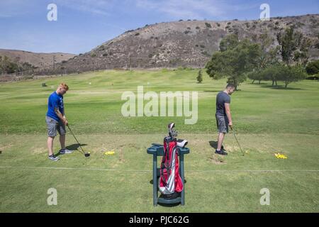 U.S. Marine Corps Lance Cpls Dylan Stovall and Jacob Grawe, recovering service members, Wounded Warrior Battalion-West, execute golf strokes at the Marine Memorial Golf Course on Marine Corps Base Camp Pendleton, California, July 16, 2018. During the practice, the Marines focused on golfing fundamentals while using various golf clubs. Stock Photo