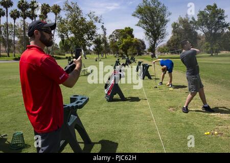 Phil Bryant, shooting and golfing coach, Wounded Warrior Battalion-West, records the form of Lance Cpls. Dylan Stovall and Jacob Grawe at the Marine Memorial Golf Course on Marine Corps Base Camp Pendleton, California, July 16, 2018. Bryant records each Marines' performance to observe improvements made and to correct deficiencies. Stock Photo