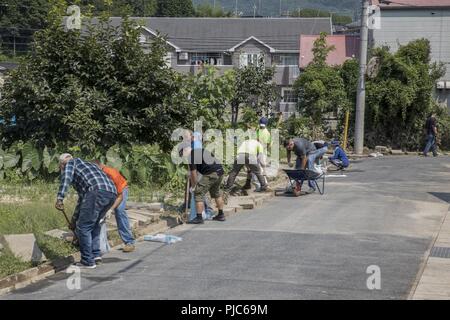 Volunteers from Marine Corps Air Station Iwakuni shovel mud and debris during a volunteer event in Hikari, Japan, July 17, 2018. The volunteer event, organized by the Marine Corps Community Services Single Marine Program, provided service members with the opportunity to help local Japanese residents clean up and recover after the area was flooded by excessive rainfall. Stock Photo