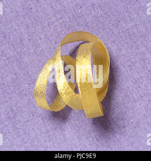 Curly gold ribbon on purple fabric background Stock Photo
